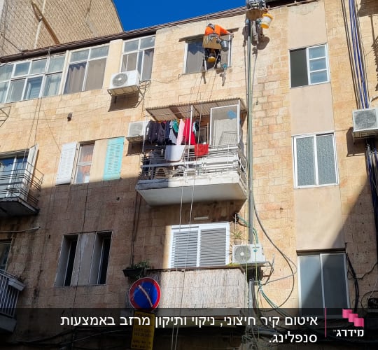 שני עובדים בגובה על חבלים צובעים קיר חיצוני